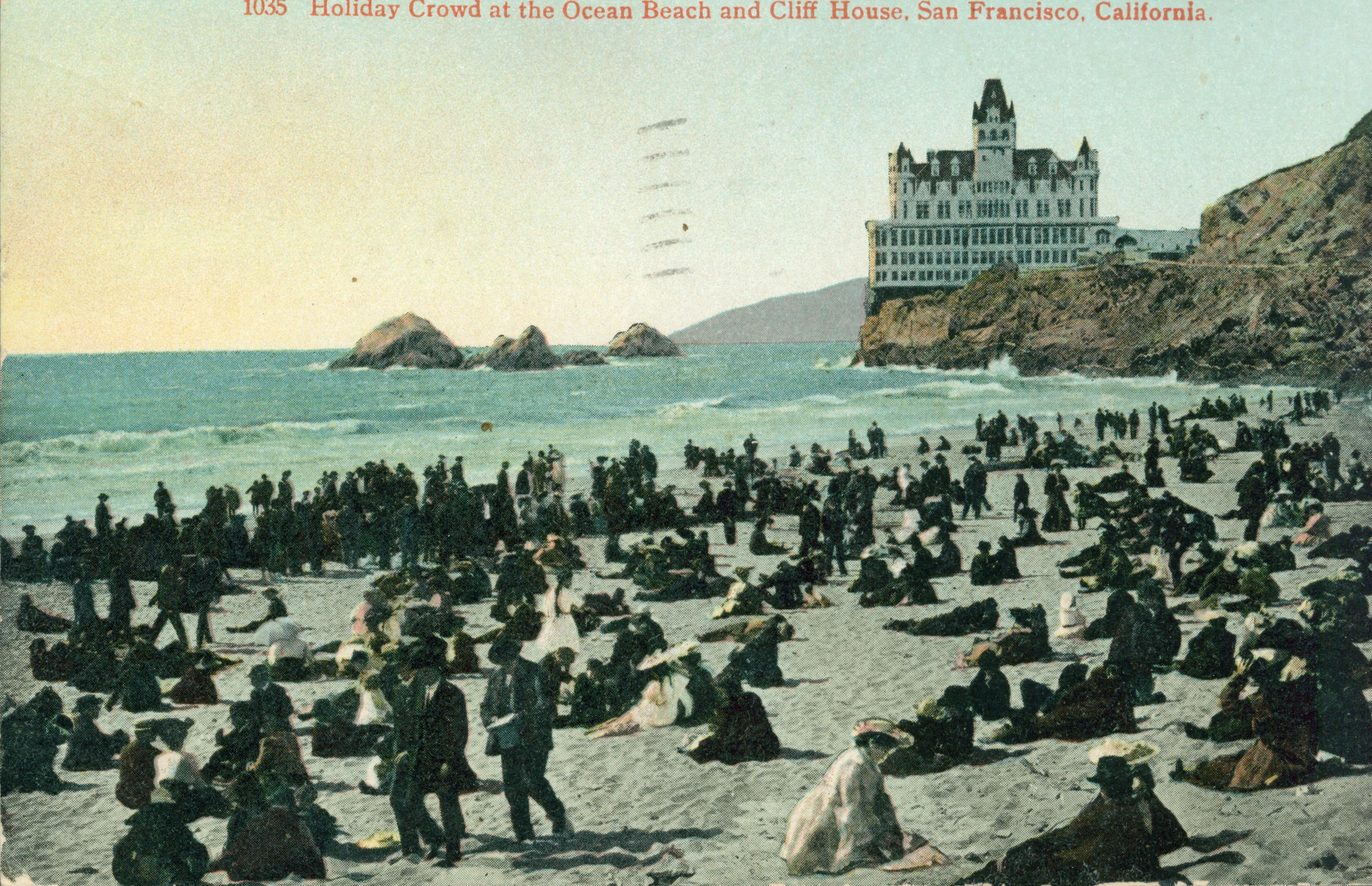 Shows the Cliff House and Seal Rocks with a large number of onlookers on the beach